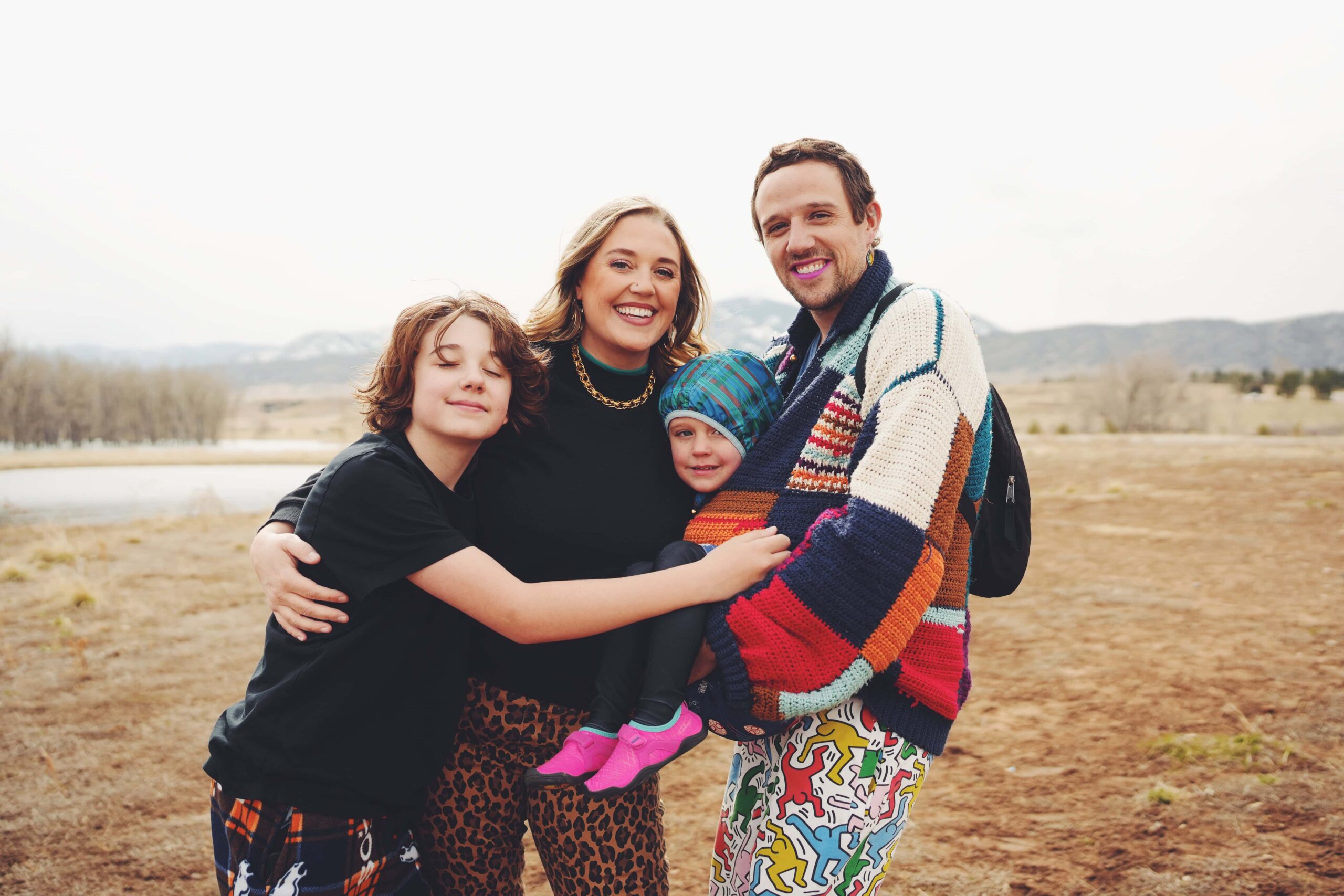 A queer family hugging in bright colored clothing smiling at their LGBTQ friendly photography session at Chatfield State Park near Denver