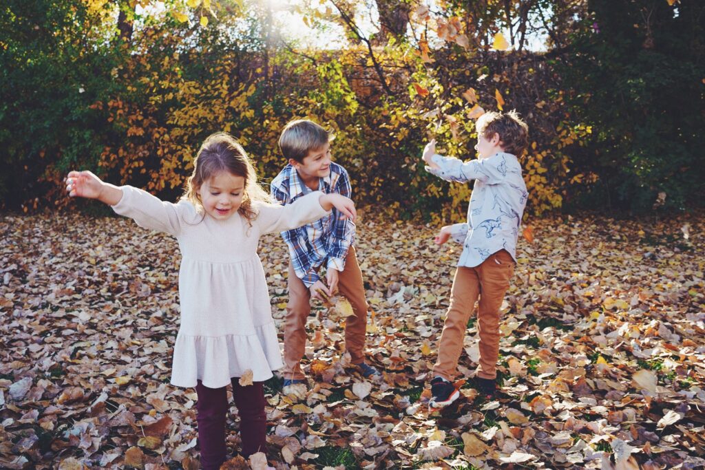 Grandkids play in the leaves at a fall extended family session at Dekovend Park in Centennial, Colorado